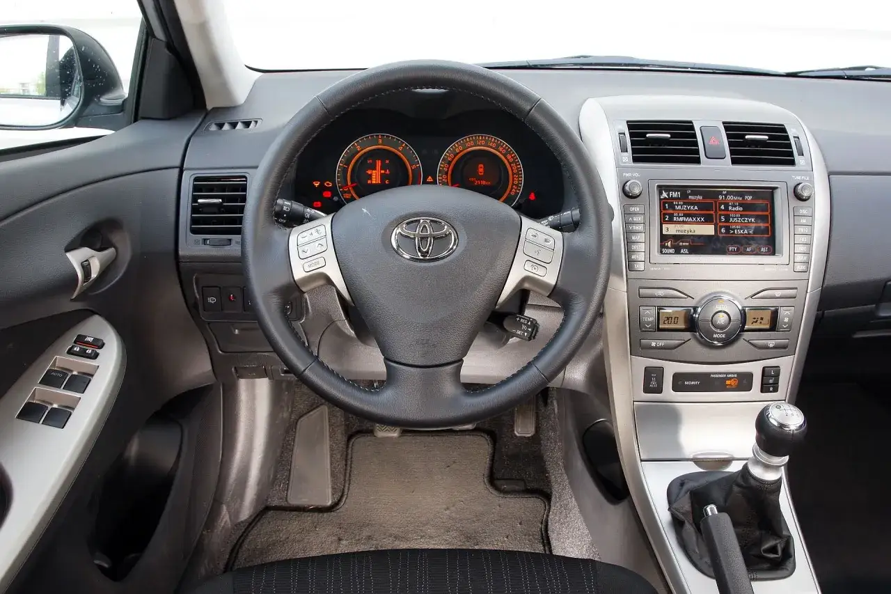 Wnętrze Toyoty Corolli 2010 z kierownicą, radiem i manualną skrzynią biegów.
