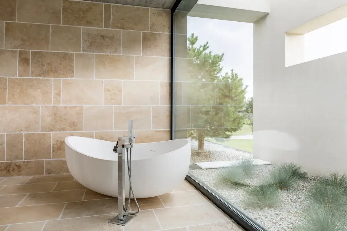 Ba&ntilde;o moderno con ba&ntilde;era exenta y gran ventanal que ofrece vistas al jard&iacute;n. Ideal para ba&ntilde;os peque&ntilde;os, maximiza la luz y la sensaci&oacute;n de amplitud.