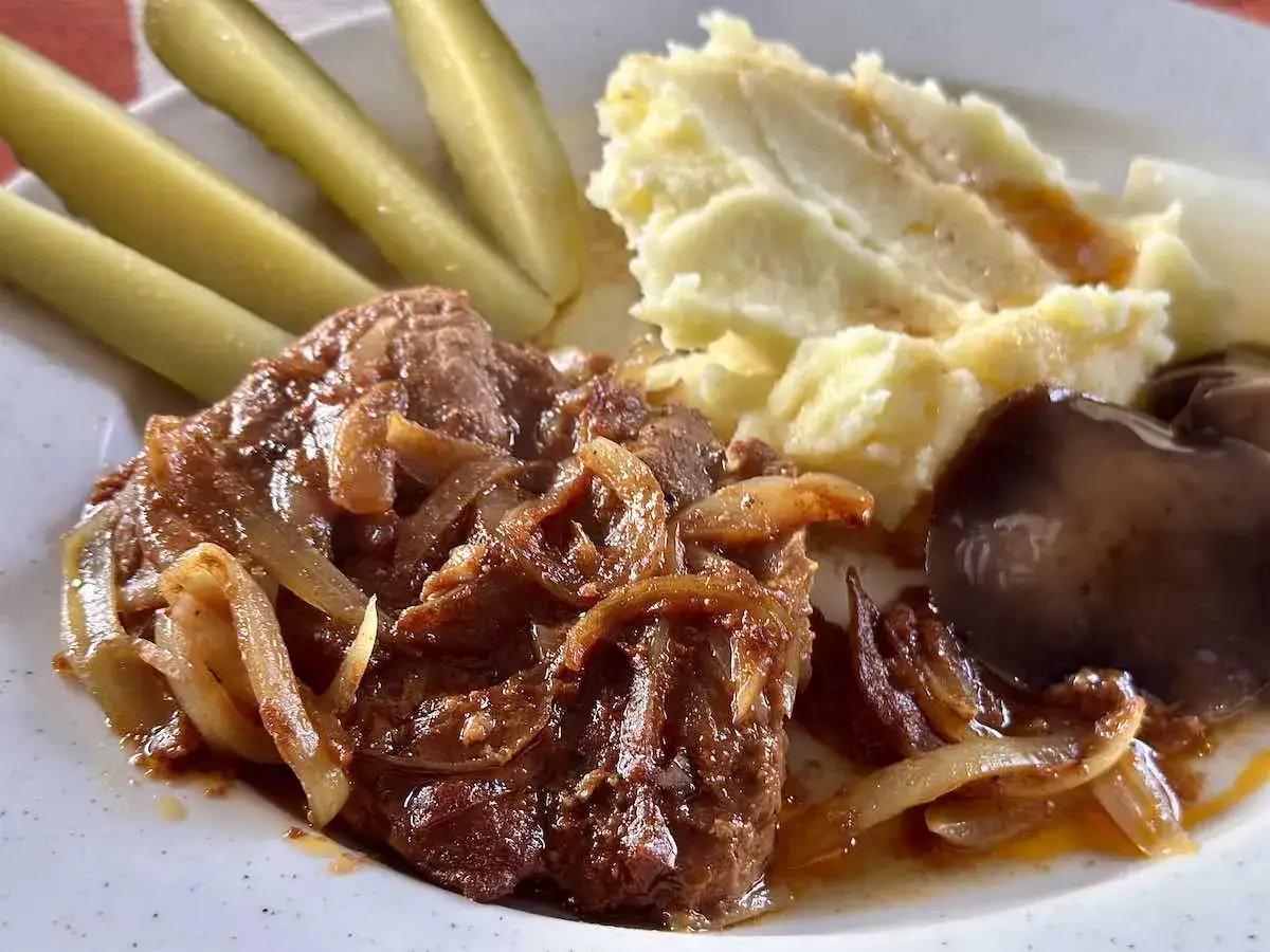 Rozpływająca się karkówka z piekarnika z cebulką, puree ziemniaczane, ogórki kiszone i grzyby.
