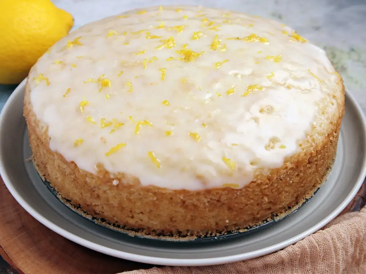 Ein saftiger veganer Zitronenkuchen mit Zuckerguss und Zitronenschale, daneben eine frische Zitrone.