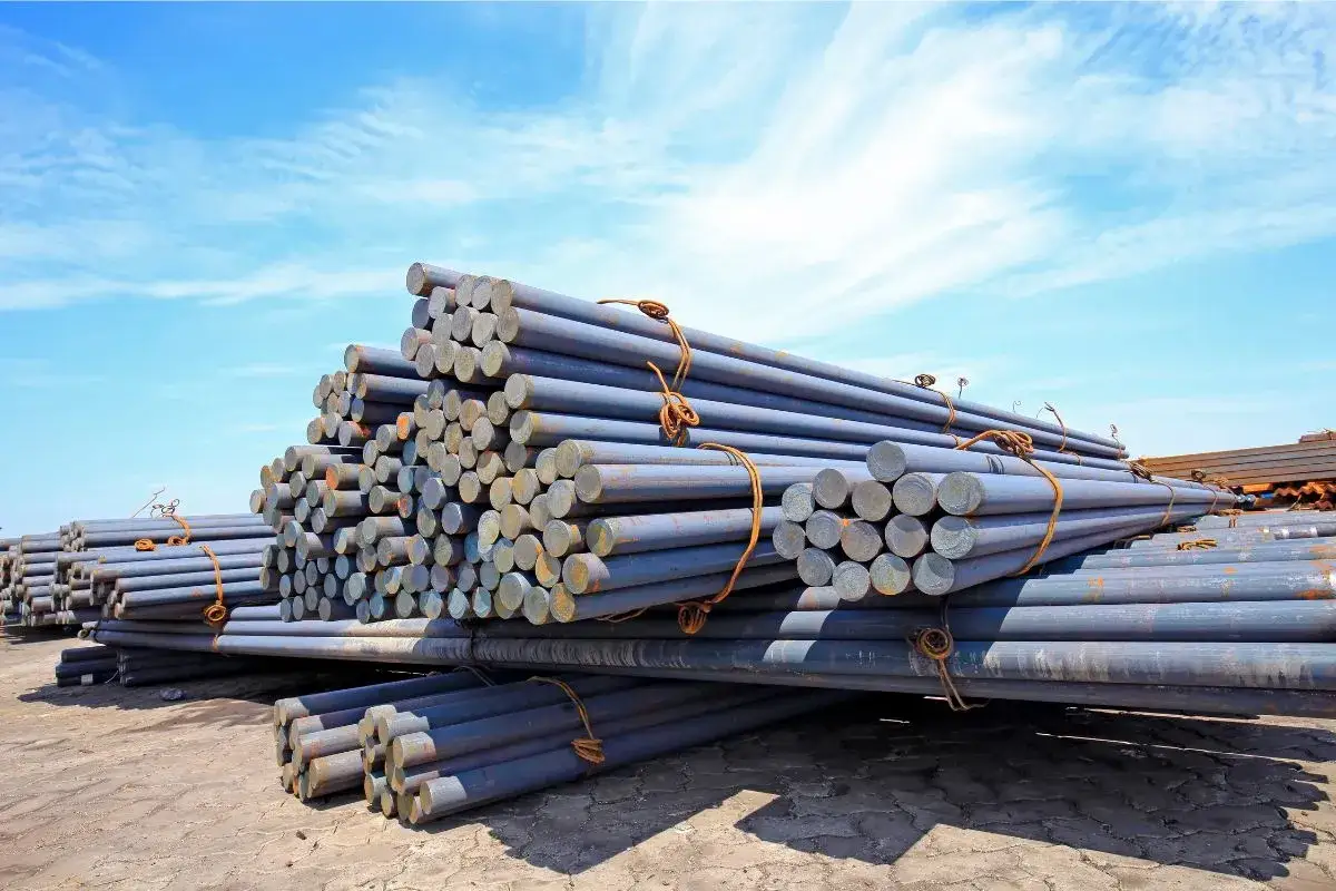 Stapel von Metallstäben, die den Unterschied zwischen Eisen und Stahl verdeutlichen. Sie liegen unter blauem Himmel.