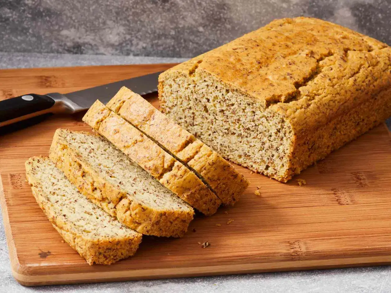 Ein frisch gebackenes low carb brot rezept, auf einem Holzbrett angeschnitten, daneben ein Messer.