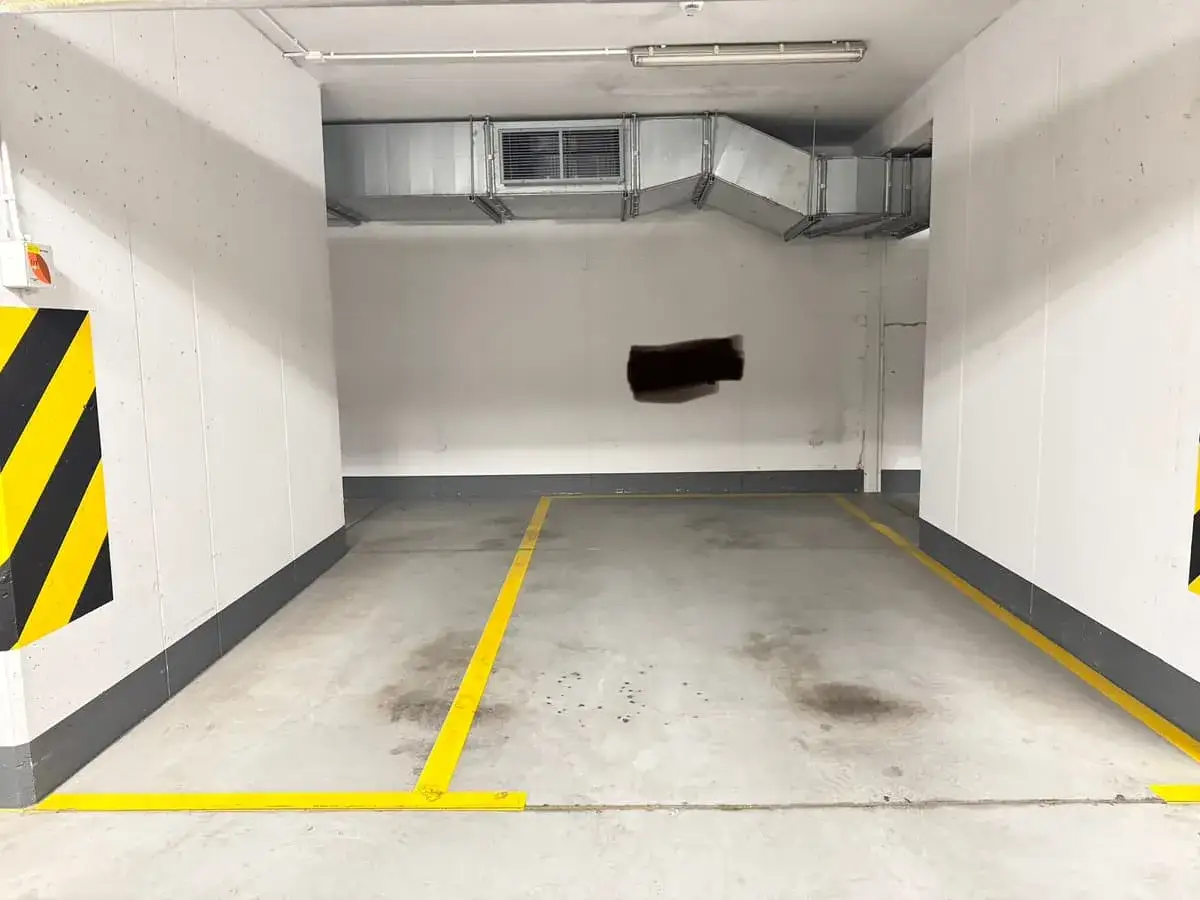 Puste miejsce parkingowe w garażu podziemnym, idealne pod wynajem. Oznaczone żółtymi liniami, z zabezpieczeniami na ścianach.