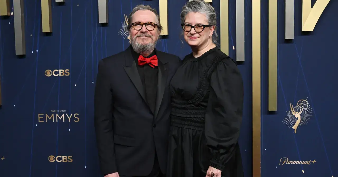 Gary Oldman z żoną na gali Emmy. Aktor w czarnym garniturze z czerwoną muszką, jego żona w czarnej sukni.