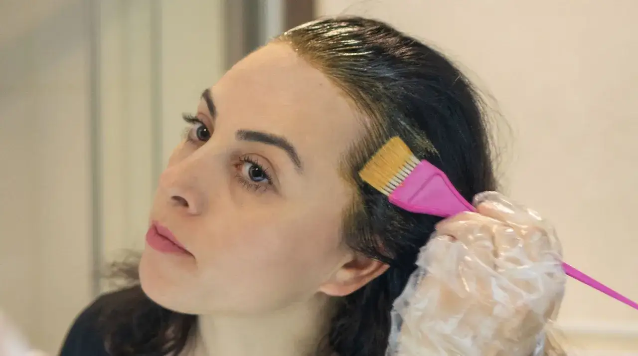 Mujer se aplica tinte pelo con brocha rosa. El tiempo de espera para el resultado es clave.
