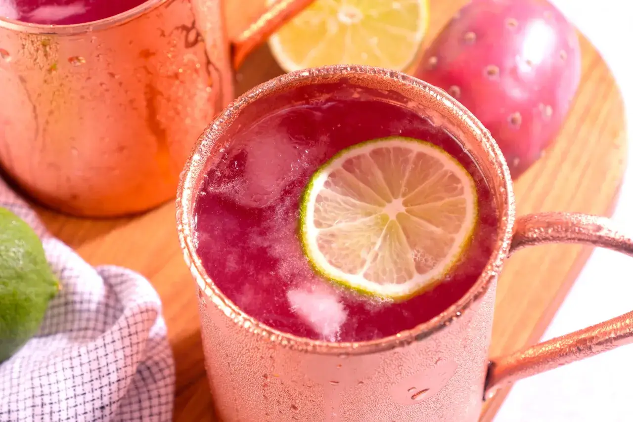 Orzeźwiający drink z wódką z kaktusa, ozdobiony plasterkiem limonki, w miedzianym kubku. Obok leżą owoce kaktusa i limonka.