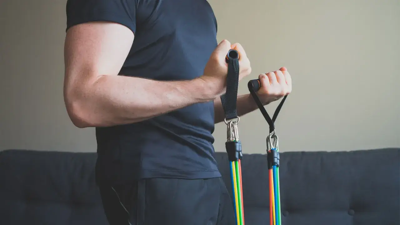 Mężczyzna wykonuje ćwiczenia na biceps i triceps z kolorowymi gumami oporowymi.