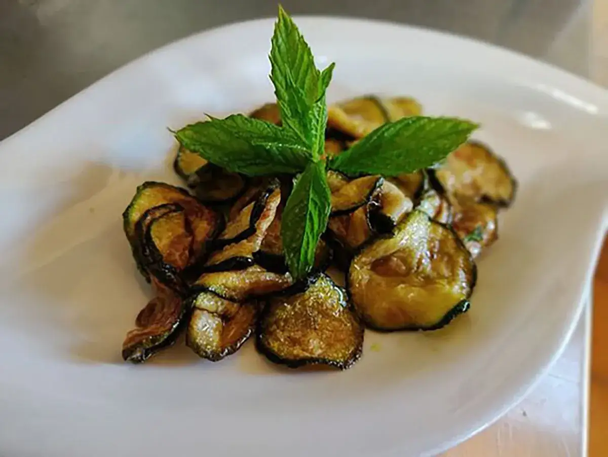 Zucchine alla scapece dorate e croccanti, guarnite con foglie di menta fresca su un piatto bianco.
