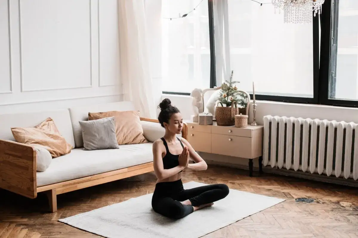 Mujer en posición de loto en una alfombra, practicando yoga. Su expresión serena refleja el sadhana significado: una práctica espiritual para alcanzar la unión.