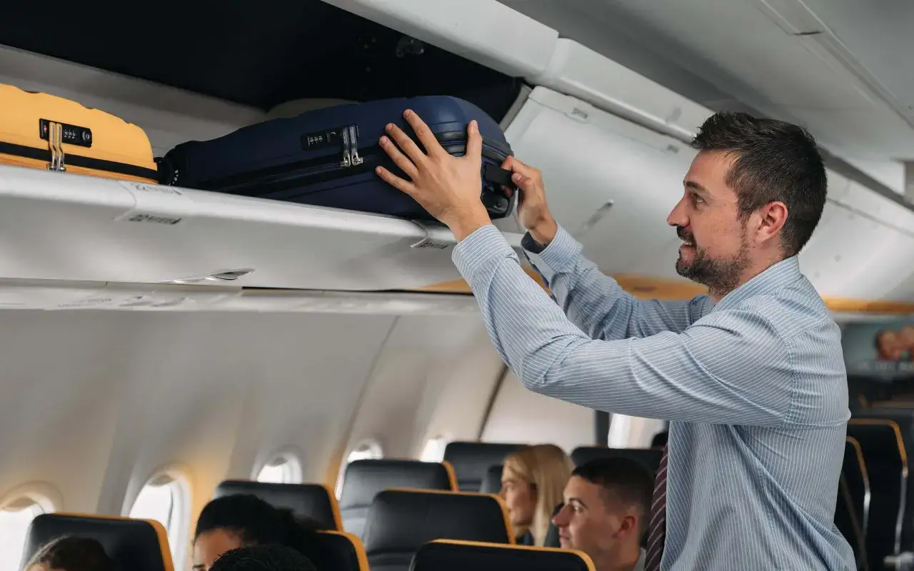 Mężczyzna w paski wkłada walizkę do schowka nad głową w samolocie Ryanair.