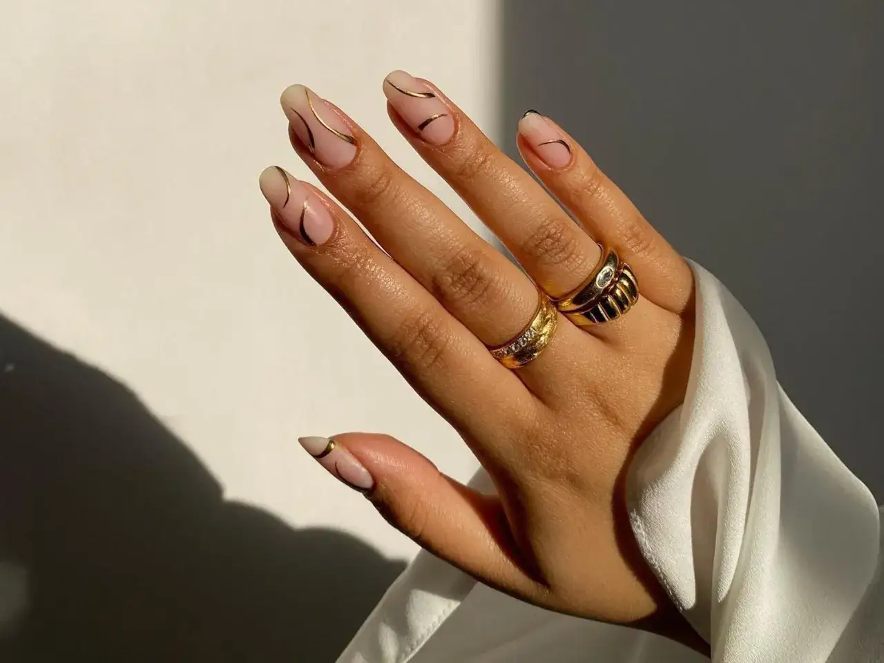Eleganta naglar med guld nagellack och tunna linjer. Två guldringar pryder fingrarna.