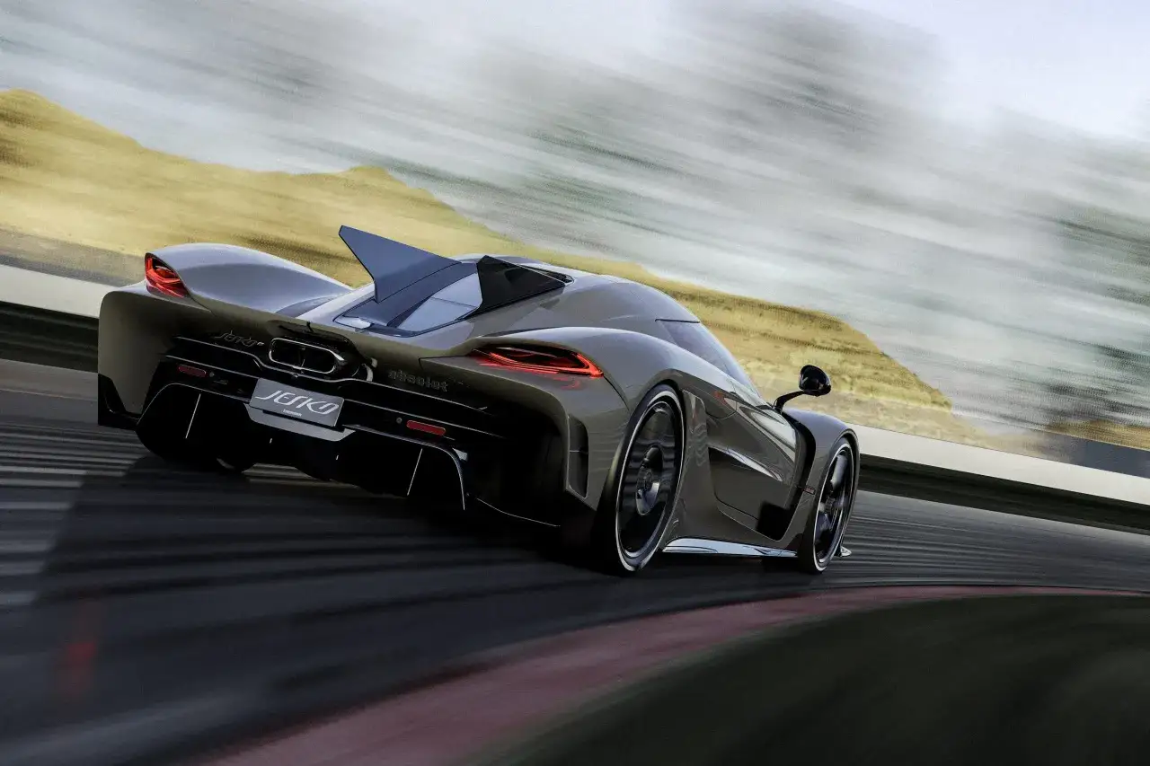 Ciemnoszary Koenigsegg Jesko Absolut pędzi po torze wyścigowym, jego sylwetka rozmyta przez prędkość na tle pustynnego krajobrazu.