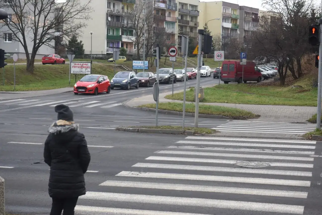 Kobieta czeka na pasach, stosując zasadę ograniczonego zaufania wobec samochodów na drodze.