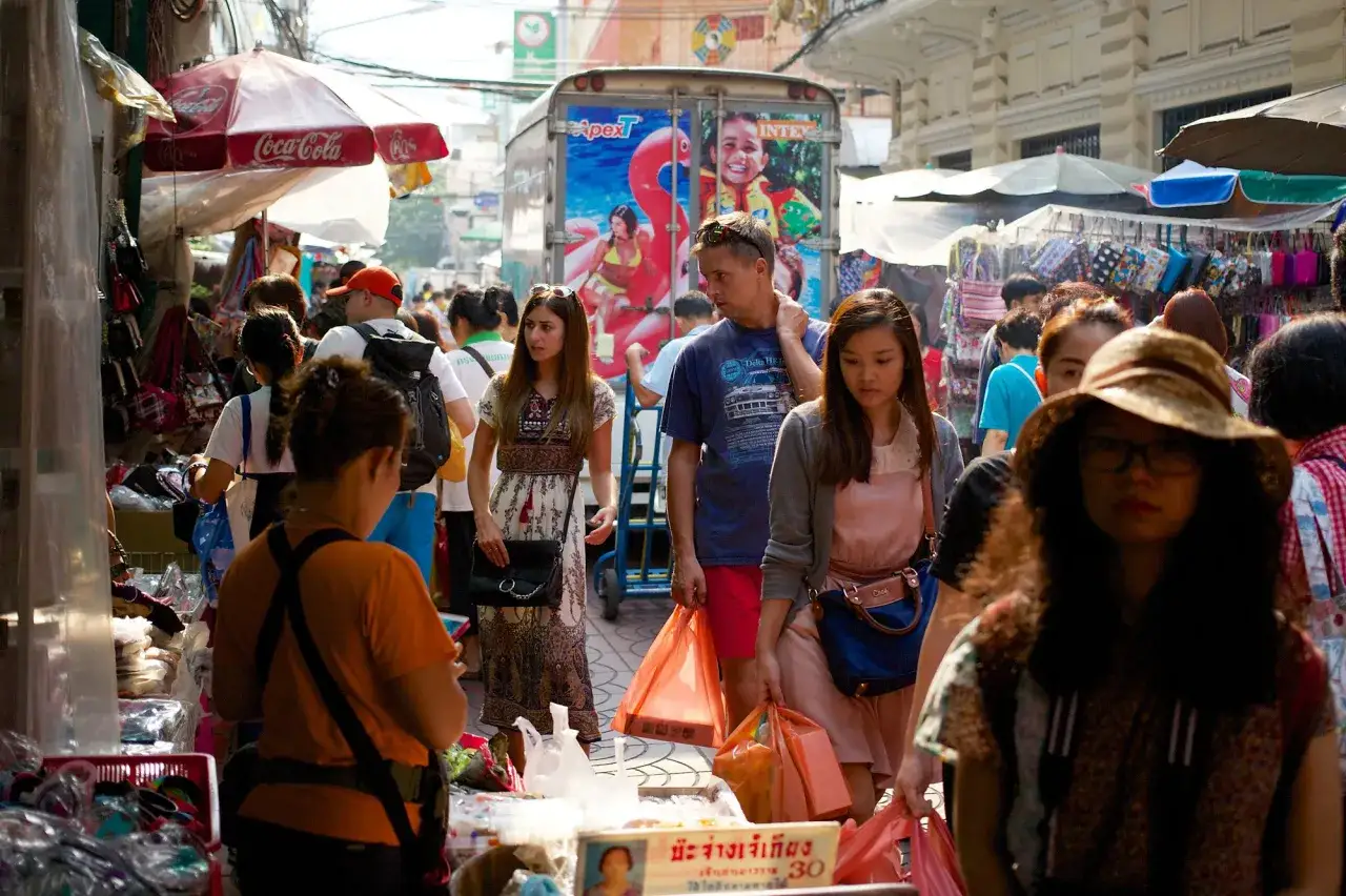 A busy street market scene captured with a 24mm lens. People shop under Coca-Cola umbrellas, with a truck featuring inflatable toys in the background.