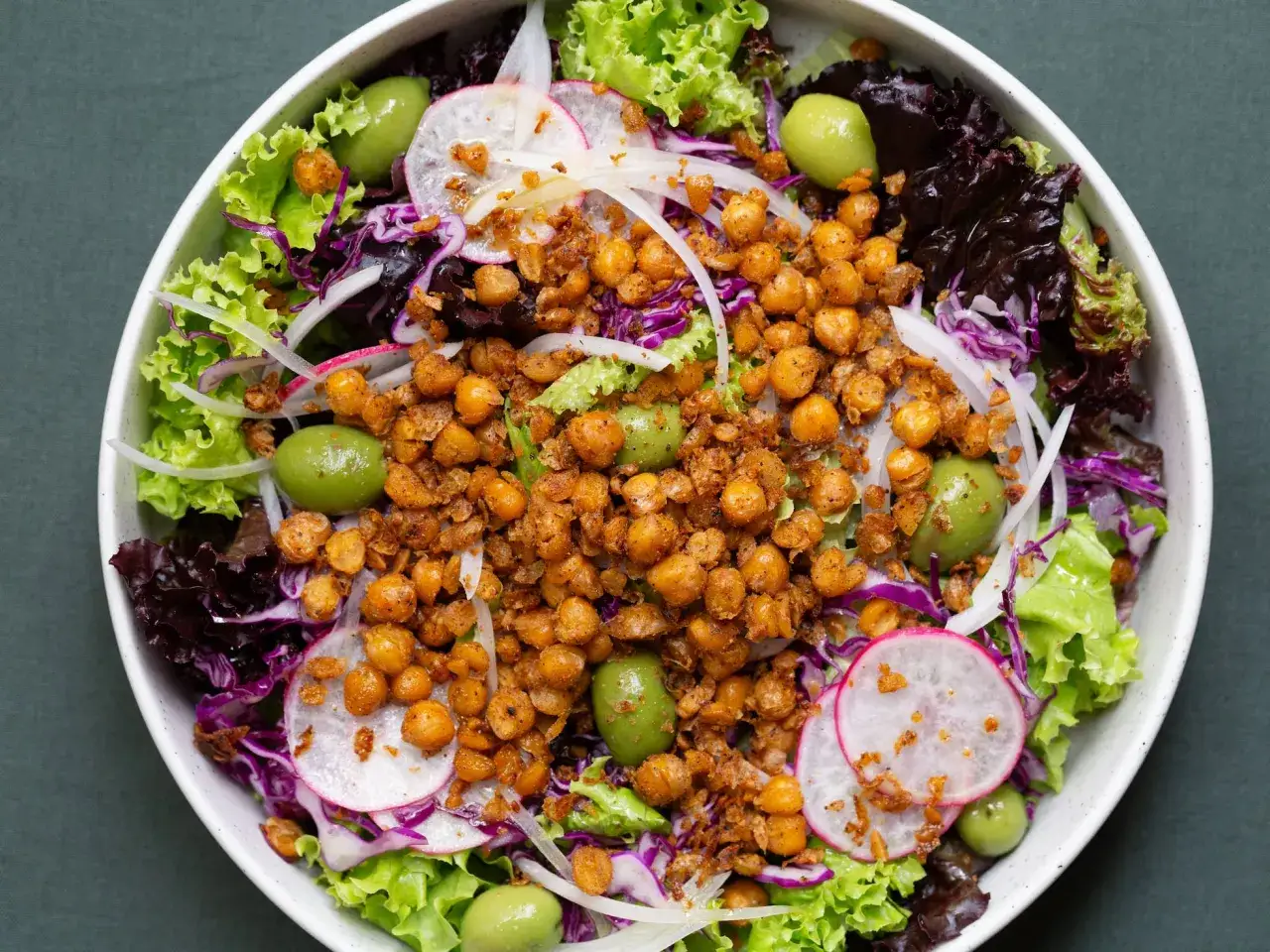 Ensalada colorida con garbanzos fritos crujientes, aceitunas verdes, lechugas variadas, r&aacute;bano y cebolla morada.