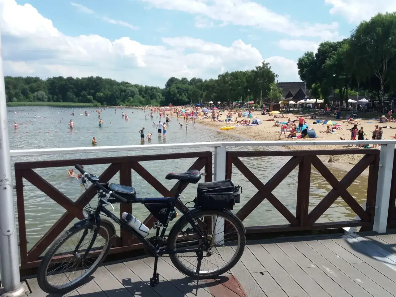 Rower na pomoście nad jeziorem Przeczyckim, gdzie plażowicze kąpią się i opalają w słoneczny dzień.