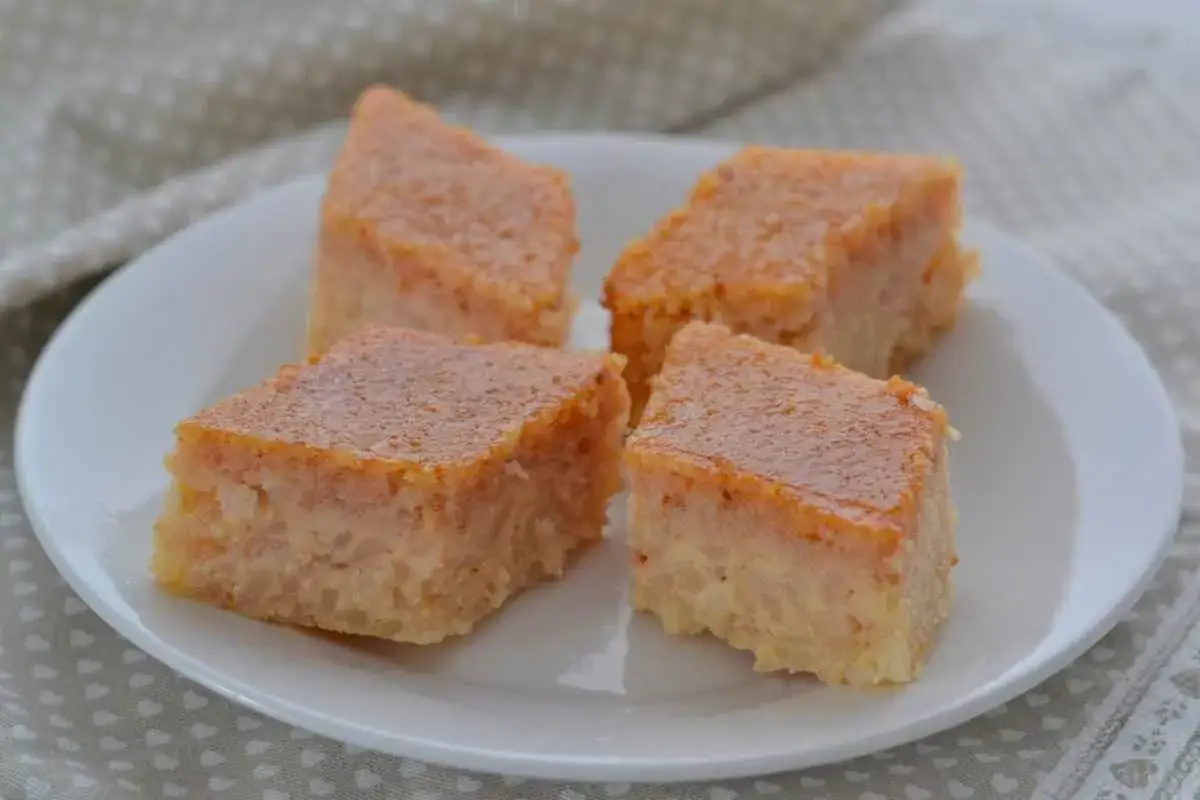 Quattro fette di torta di riso, con la crosticina dorata, servite su un piatto bianco. La torta di riso ricetta originale, un dolce cremoso e profumato.