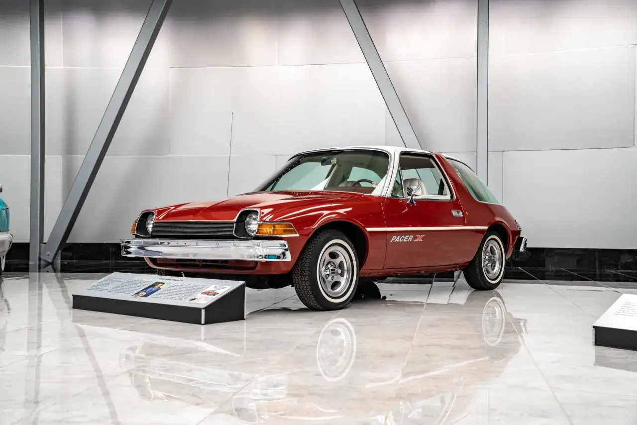 Röd AMC Pacer X med vitt tak står på ett glänsande golv. Bilen har en unik, rundad design.