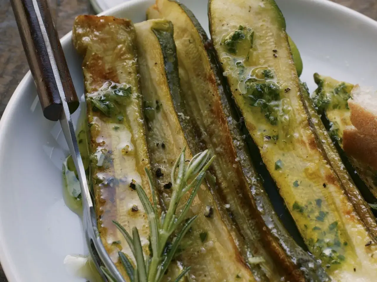 Gegrillte Zucchinischeiben mit Kräutern und Öl, perfekt zum Marinieren. Ein Rosmarinzweig liegt daneben.