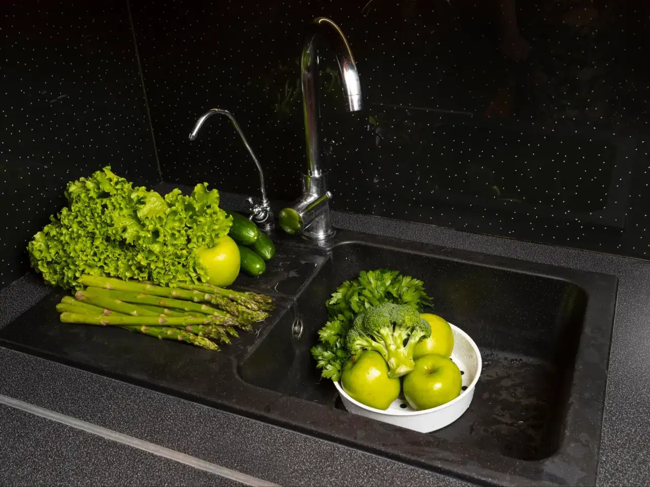 Zielone warzywa i owoce w czarnym zlewie. Zastanawiasz się, czym wyczyścić czarny zlew? Ten obrazek sugeruje, że nawet w takim zlewie można przygotować świeże produkty.
