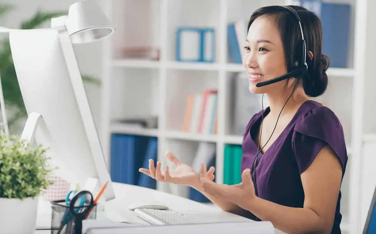 Frau mit Headset am Schreibtisch, die gestikuliert. Sie findet neue jobs mit menschen quereinstieg.
