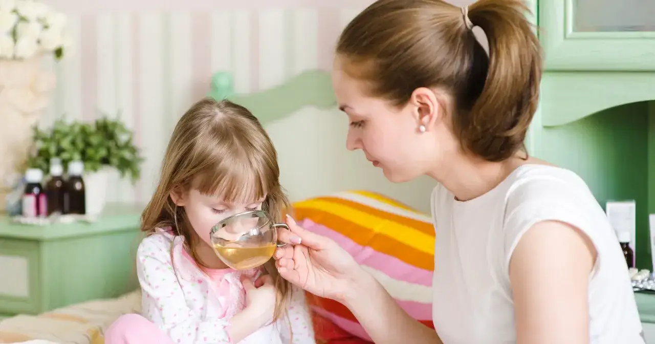 Mama podaje chorej córce herbatę z lipy. Czy dzieci mogą pić herbatę z lipy? Tak, to naturalny sposób na przeziębienie.