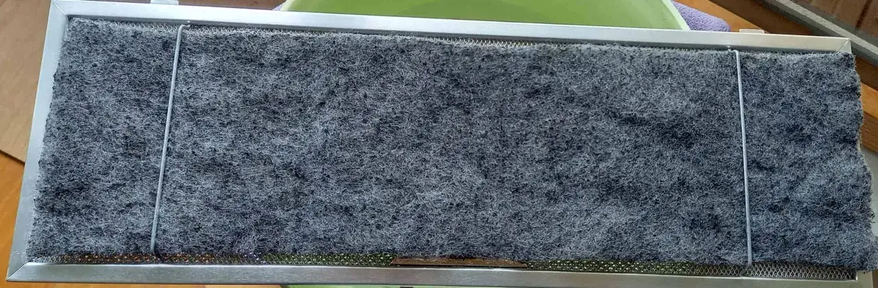 Filtre à charbon de hotte aspirante, prêt à nettoyer. Il est composé d'une grille métallique et d'une épaisse couche de matériau filtrant gris.