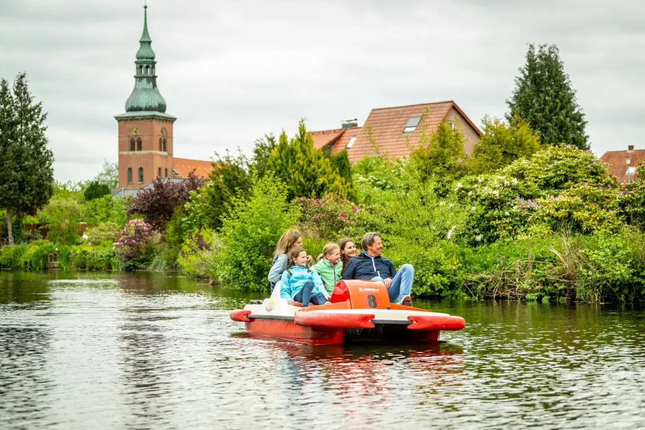 Familie genie&szlig;t eine Bootsfahrt auf dem Bruchsee Duingen. Im Hintergrund eine Kirche und gr&uuml;ne B&auml;ume.