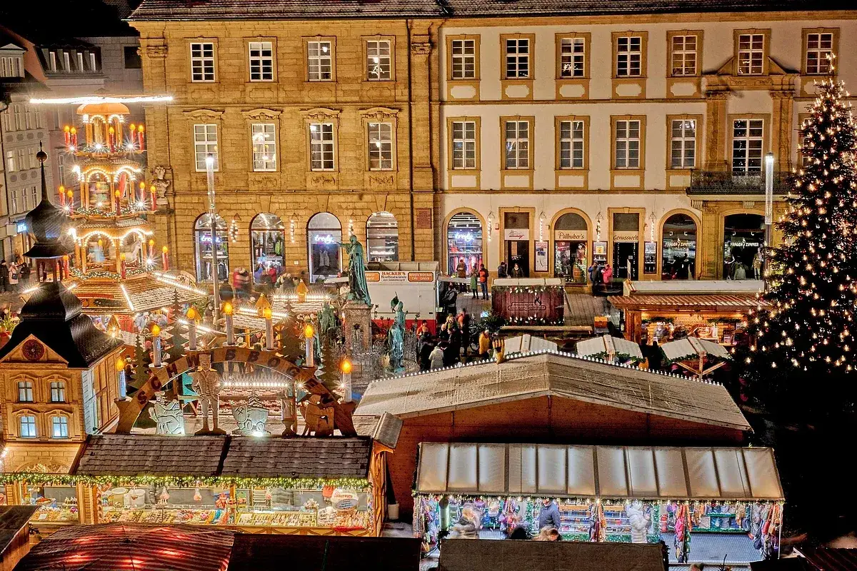 Bamberg feste: Ein beleuchteter Weihnachtsmarkt mit Pyramide, Buden und geschm&uuml;cktem Baum vor historischen Geb&auml;uden.