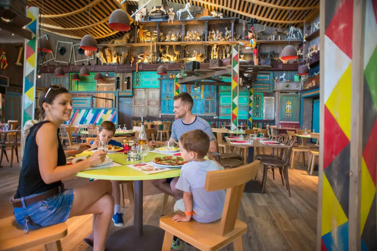 Familie genie&szlig;t Pizza in einem bunten Center Parcs Restaurant mit vielen Dekorationen an den W&auml;nden.