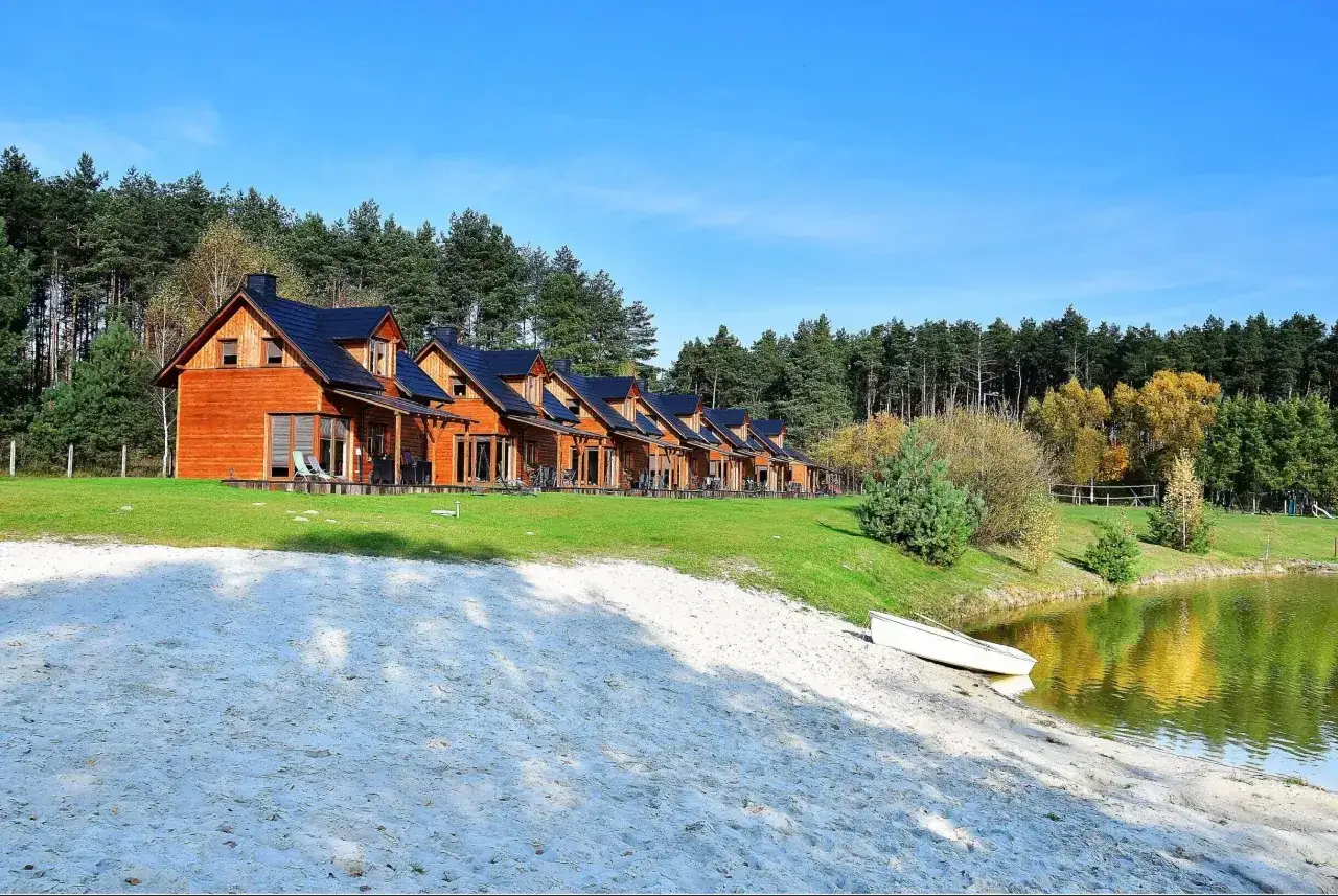 Agroturystyka z wędkowaniem Wielkopolska: drewniane domki nad jeziorem, piaszczysta plaża i las. Idealne miejsce na relaks i łowienie ryb.