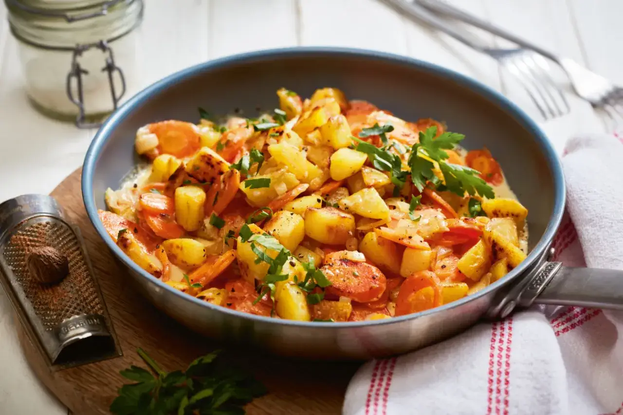 Kartoffeln mal anders: Ein herzhaftes Gericht aus goldbraunen Kartoffelwürfeln und Karottenscheiben in cremiger Sauce, garniert mit frischer Petersilie.