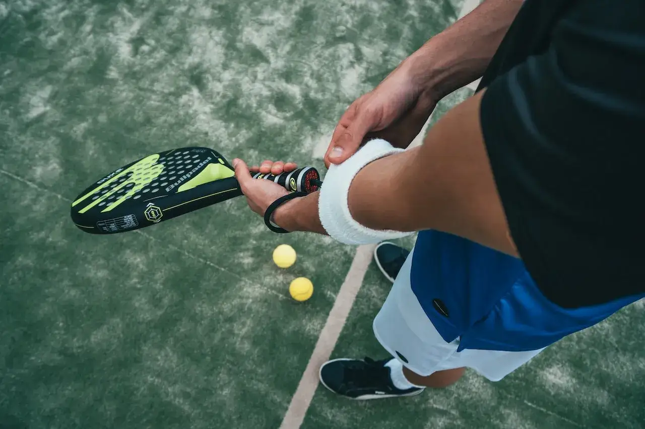 Giocatore di padel pronto a colpire la palla, con un movimento di split step. Due palline gialle sul campo verde.