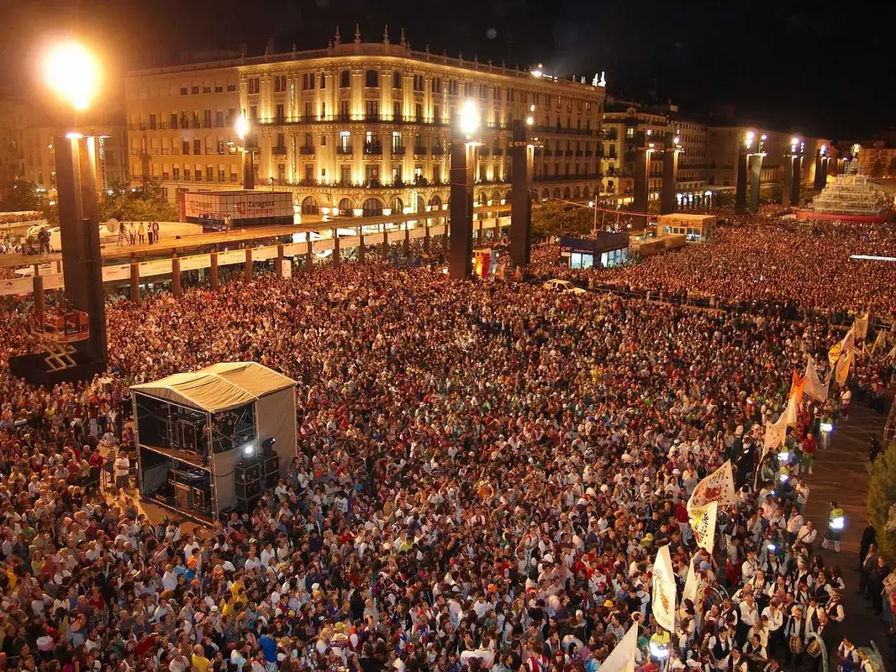 Multitudinaria plaza abarrotada para la fiesta de los **Pilares**. Luces, escenario y gente celebrando.