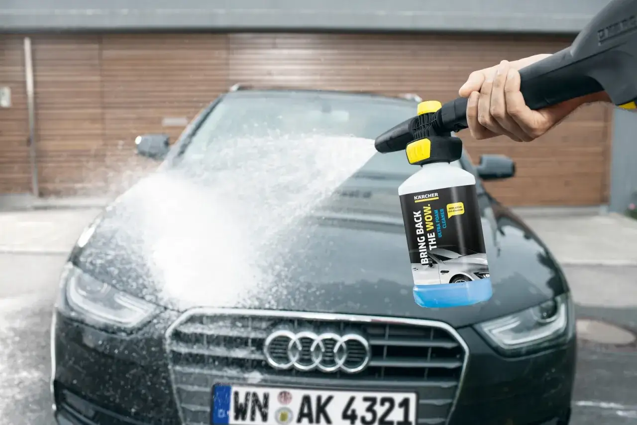 En hand sprutar Kärcher bilschampo på en mörk Audi. Skummet täcker bilens front.