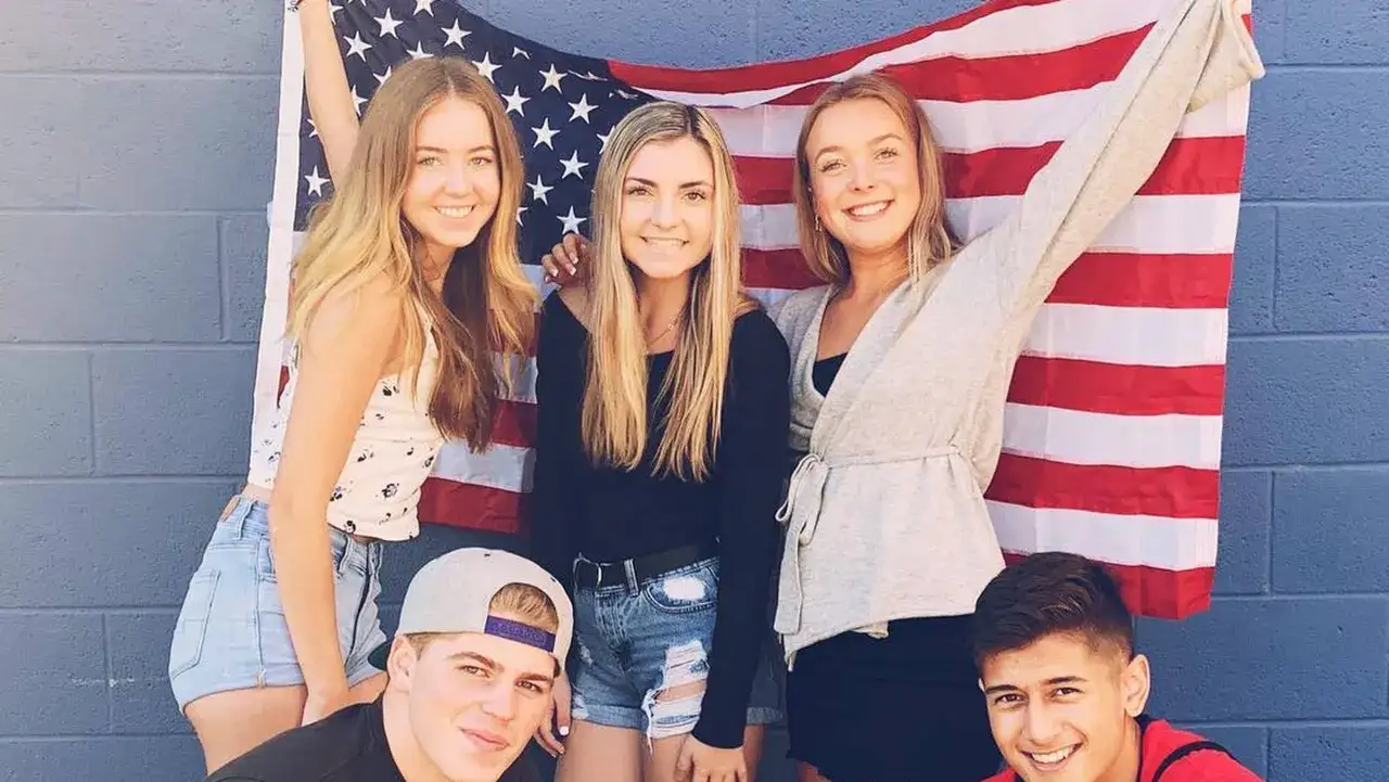 F&uuml;nf Freunde feiern ihr High School Jahr in den USA vor einer amerikanischen Flagge.