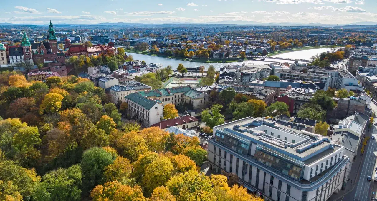 Widok na jesienny Kraków z wieżami Wawelu i Wisłą. W oddali nowoczesny budynek, być może Radisson Blu Hotel Krakow.