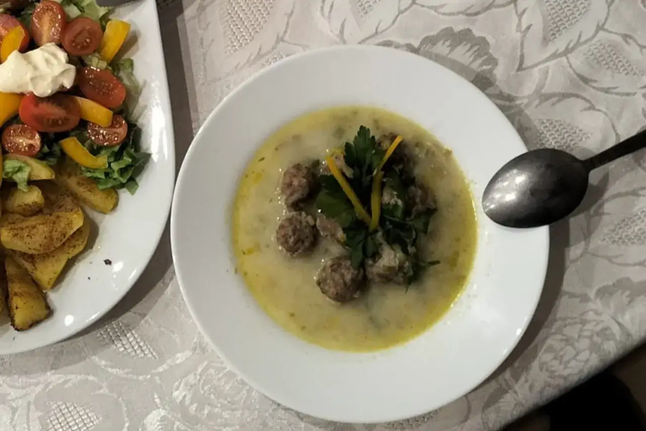 Aromaticzna zupa porowo serowa z pulpecikami, udekorowana natką pietruszki i skórką cytryny. Obok talerz z sałatką i frytkami.