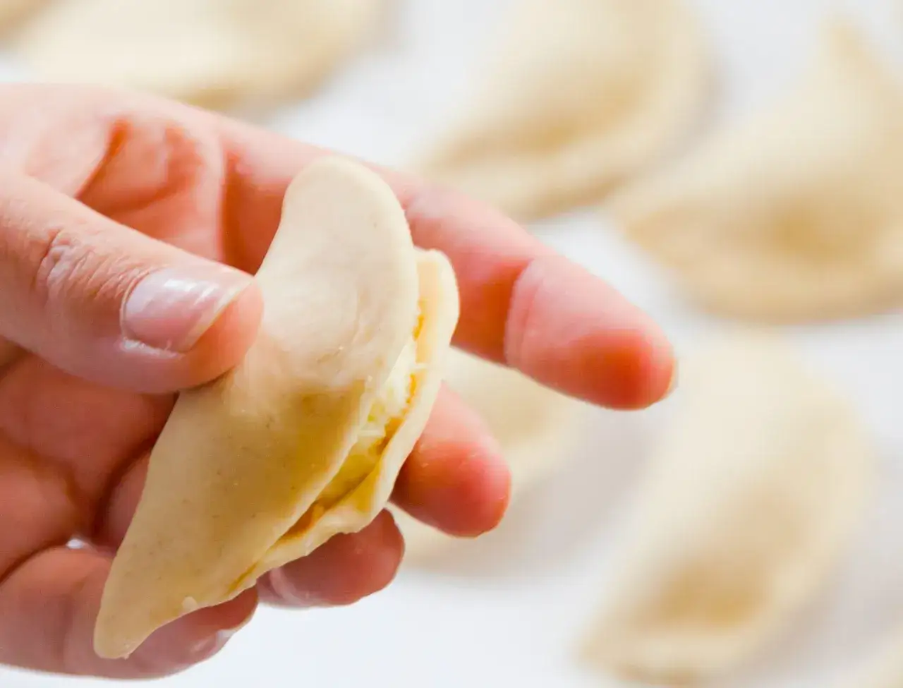 Ręka formuje pieroga, przygotowując go do gotowania. To kluczowy etap w przepisie na pierogi, który wymaga precyzji.