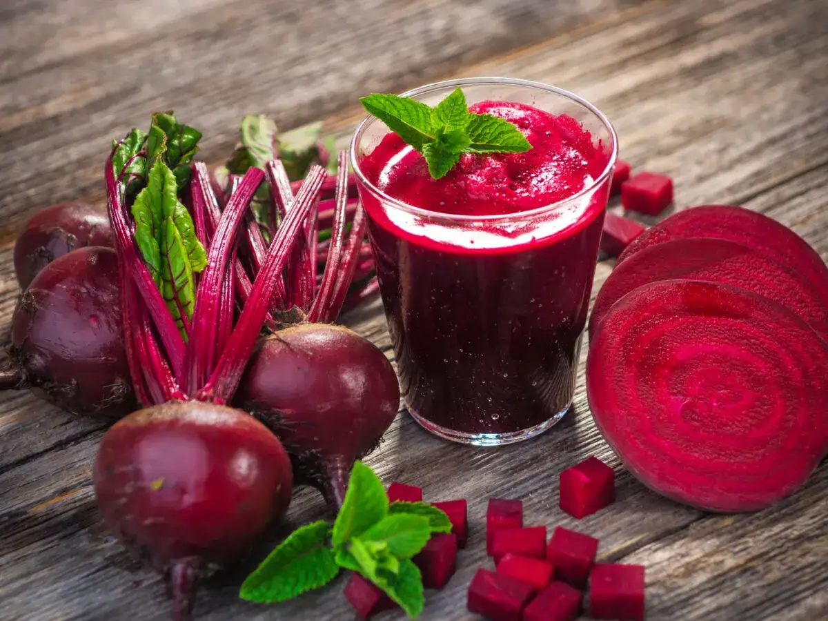 Frischer Rote Bete Saft, der für eine gesunde Erektion sorgen kann, neben ganzen und geschnittenen Rote Bete auf Holz.