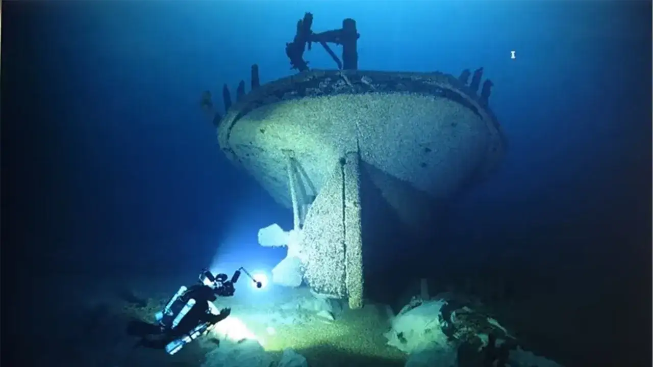 Ein Taucher erkundet einen **gesunkenen Schiff**-Wrack, dessen Heck im blauen Wasser aufragt.