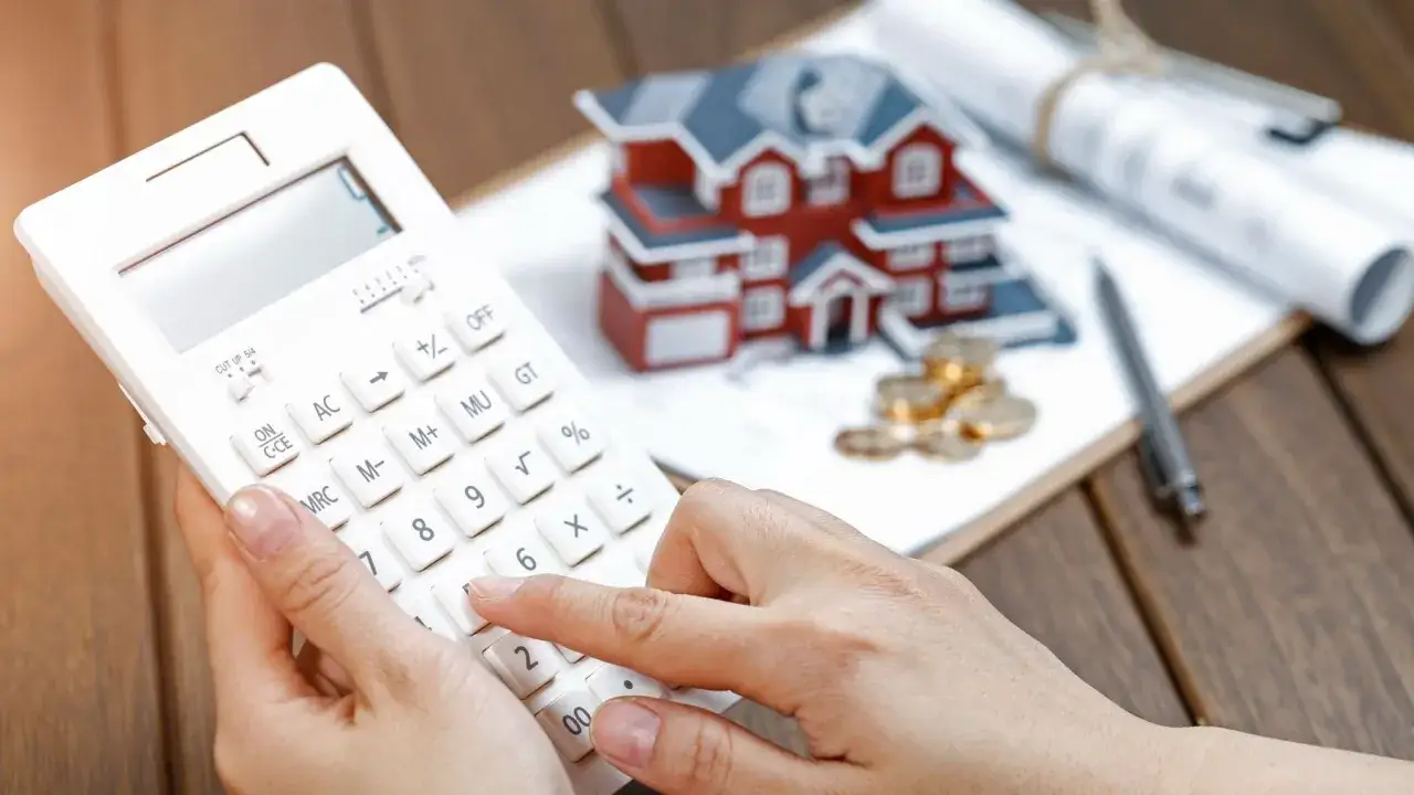 Calculando la casilla 435 renta. Una mano usa una calculadora blanca junto a una maqueta de casa, monedas y planos.