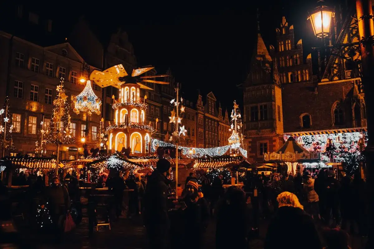 Wrocław jarmark nocą. Rozświetlone choinki, karuzela i wielka, wielopoziomowa piramida tworzą magiczną atmosferę. Tłumy ludzi spacerują między straganami.