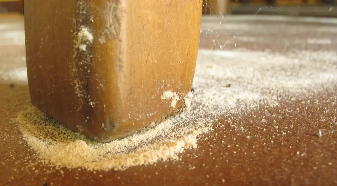 Polvo fino alrededor de una pata de madera, indicando la necesidad de eliminar carcoma.
