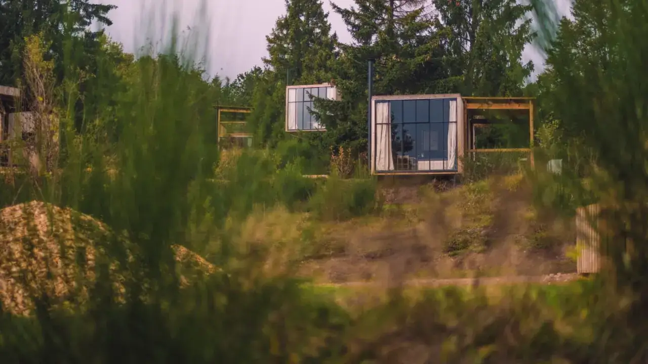 Trois cabanes modernes avec de grandes fenêtres, nichées dans la verdure. Un exemple de logement insolite grand est, offrant une immersion dans la nature.