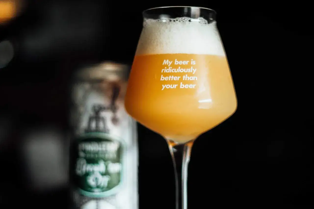 Bicchiere con birra neipa dal colore dorato e schiuma abbondante. Sul vetro la scritta 