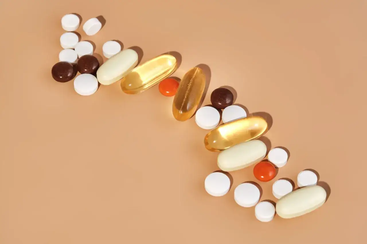 En samling piller och kapslar, inklusive guldfärgade omega-3, vita och bruna tabletter, samt orange kapslar. Dessa kan vara en del av ett antiinflammatorisk kosttillskott.