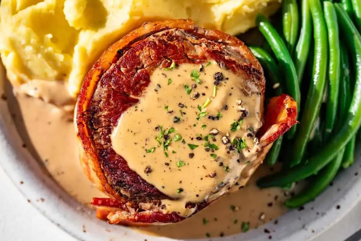En saftig biff insvept i bacon, toppad med krämig pepparsås. Serveras med potatismos och gröna bönor. Ett perfekt pepparsås recept för en lyxig middag.