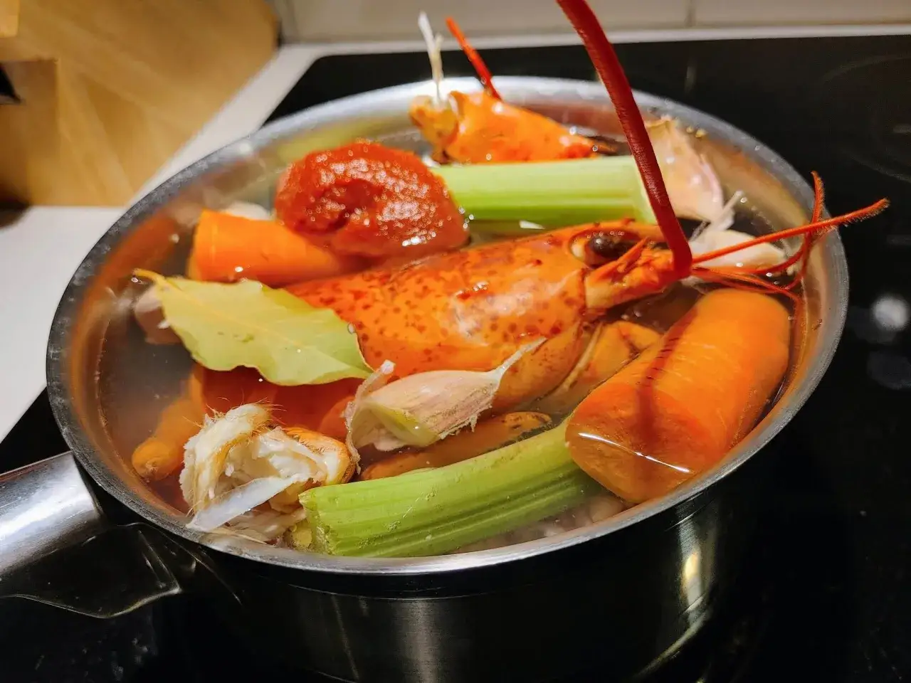 Cuisson homard vivant dans un bouillon aromatique avec carottes, céleri, ail et feuille de laurier.
