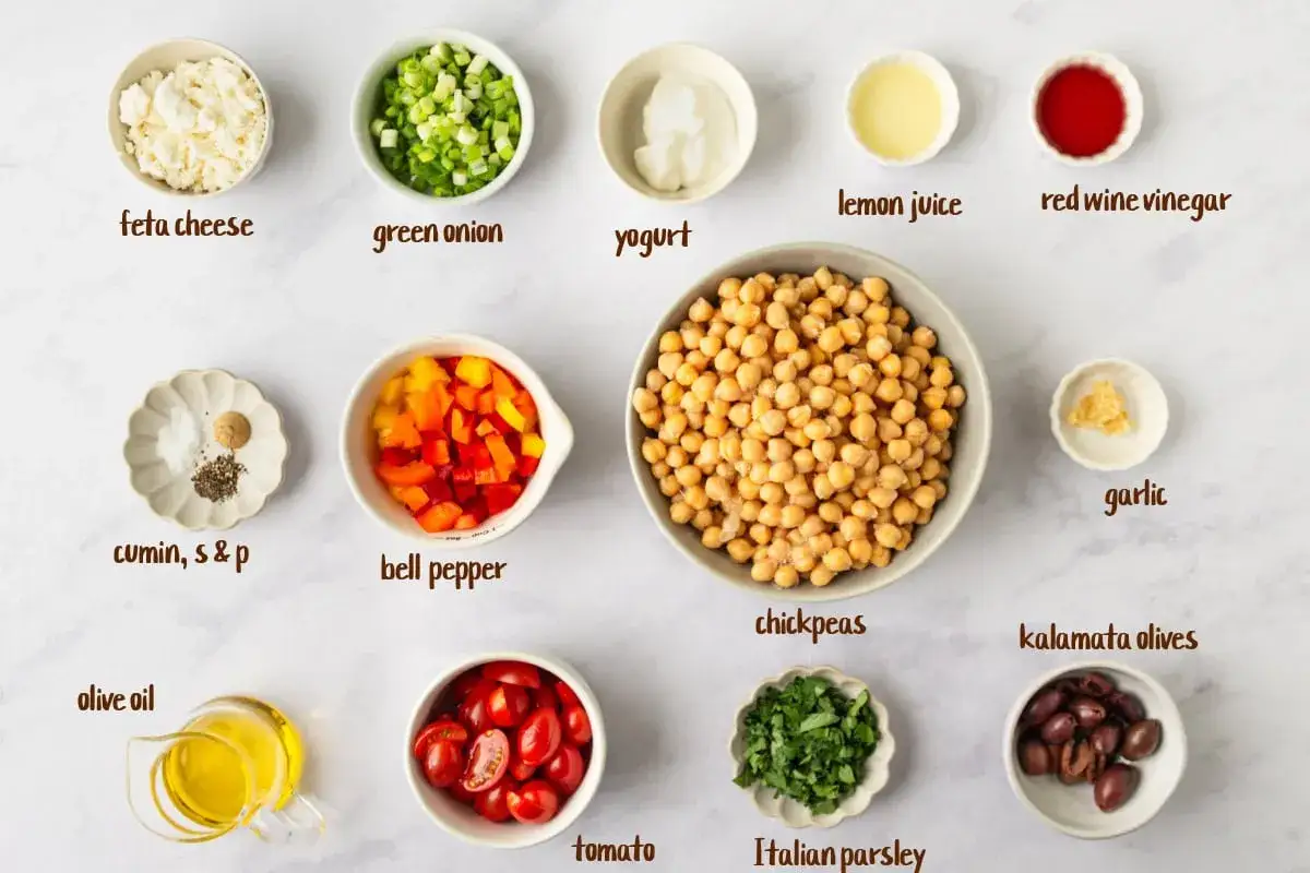 Zutaten für einen leckeren Kichererbsen Salat: Kichererbsen, Feta, Paprika, Tomaten, Oliven, Zwiebeln, Knoblauch, Petersilie, Joghurt, Olivenöl, Zitronensaft, Essig, Kreuzkümmel, Salz & Pfeffer.